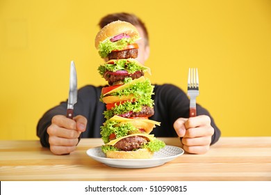 Man Eating Huge Burger At Table