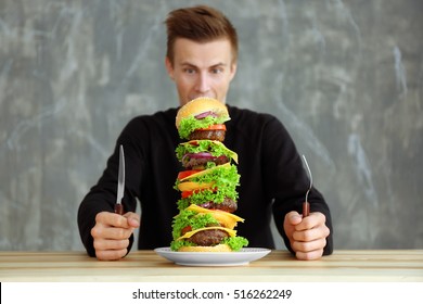 Man Eating Huge Burger At Table