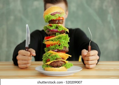 Man Eating Huge Burger At Table