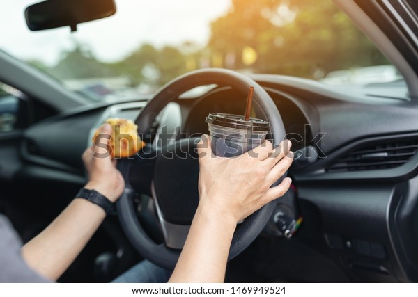 Man\
eating a pizza and drinking coffee while driving\
car.