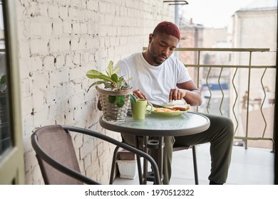 Man eating with pleasure scrambled eggs and toasts during the breakfast at the balcony