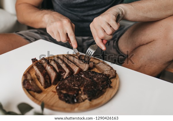 A man eating rib eye steak from a wooden plate -\
Carnivore Diet