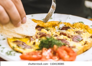 Man Eating Scrambled Eggs And Bacon Served With Herbs And Tomato.