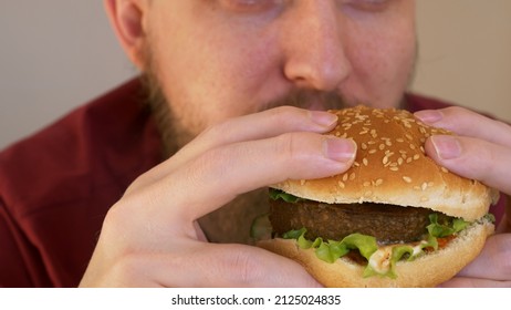 Man Eating Vegan Hamburger. Junk Food Alternative, Healthy Fast Food Concept. Burger In Male Hands. A Bearded Man Eats A Delicious Hamburger Or Cheeseburger With A Thick Fat Cutlet.