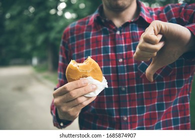 A man eats a hamburger and he doesn’t like it. He shows a finger down.