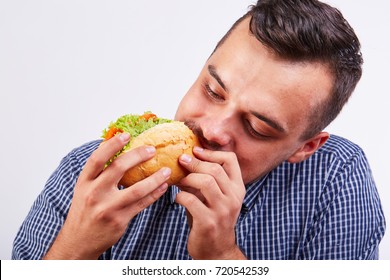 A man eats a large mouth-watering hot dog with tomatoes and lettuce leaves.