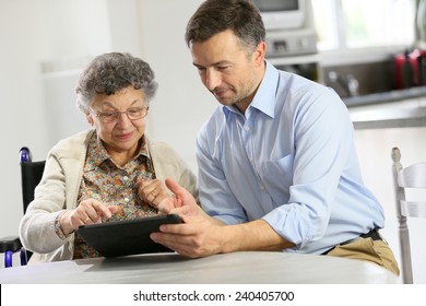 Man With Elderly Woman Using Digital Tablet