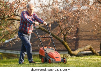 Man with electric lawnmower, lawn mowing. Gardener trimming a garden. Sunny day, suburb, village. Adult man pruning and landscaping garden, trimming grass, lawn, paths. Hard work on nature - Shutterstock ID 1378720874