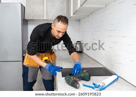 Man electrical repairs kitchen surface apartment. Installing hob in countertop. Man bought new kitchen furniture and appliances. Process installing an electrician household appliances.