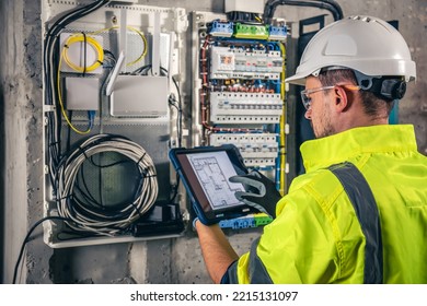 Man, an electrical technician working in a switchboard with fuses, uses a tablet. - Shutterstock ID 2215131097
