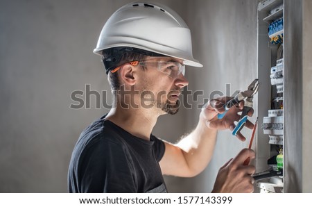 Man, an electrical technician working in a switchboard with fuses. Installation and connection of electrical equipment. Professional with tools in hand. concept of complex work, space for text.
