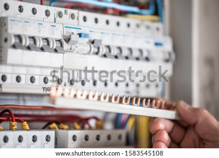 Man, an electrical technician working in a switchboard with fuses. Installation and connection of electrical equipment. Professional with tools in hand. concept of complex work, space for text.