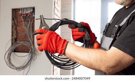 Man electrician. Hands electrification engineer. Electrician guy with wire. Cropped man installs electrical panel. Man electrician in gloves. Electrical equipment installation. Insulation, grounding