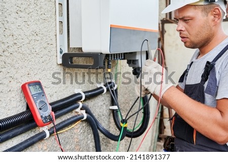 Man electrician installing solar panel system. Technician in helmet and gloves making electrical wiring inverter and electric box. Concept of alternative and renewable energy.