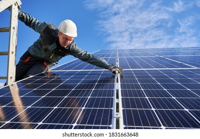 Man electrician standing on ladder and installing photovoltaic solar panels under blue cloudy sky. Technician wearing safety helmet and gloves. Concept of alternative energy and power - Shutterstock ID 1831663648