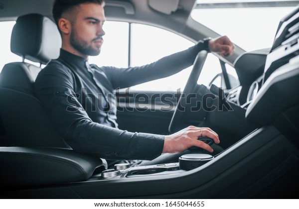 Man in elegant clothes sitting in brand new\
expencive automobile.