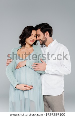 Man embracing smiling pregnant wife isolated on grey 