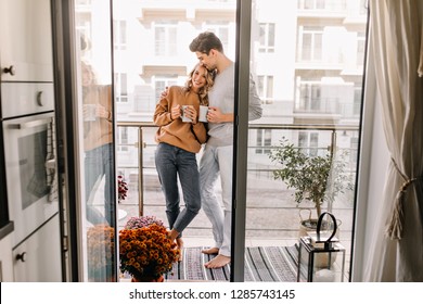 Man embracing wife at balcony. Relaxed couple drinking coffee in weekend.