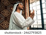 Man from emirati wearing kandura outfit spending time in an arabian traditional house in Dubai. Young man praying in the mosque.