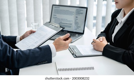 Man employer in suit is holding resume of applicant to reading her profile and asking candidate question while sitting to job interview and explaining about job description in office - Shutterstock ID 2003008232