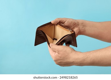 Man with empty wallet on light blue background, closeup. Space for text