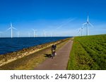A man energetically cycling down a path lined with wind turbines in the Netherlands Flevoland during the vibrant spring season. men on electric bike with windmill turbines on the background
