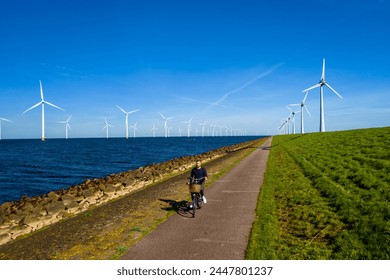 A man energetically cycling down a path lined with wind turbines in the Netherlands Flevoland during the vibrant spring season. men on electric bike with windmill turbines on the background