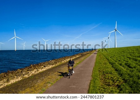 A man energetically cycling down a path lined with wind turbines in the Netherlands Flevoland during the vibrant spring season. men on electric bike with windmill turbines on the background