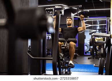 A man is engaged in a strength training session using a lat pulldown machine in a well-equipped gym. The setting features modern decor and vibrant lighting that energizes the space.
