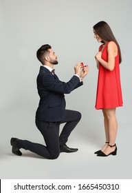 Man with engagement ring making marriage proposal to girlfriend on light grey background