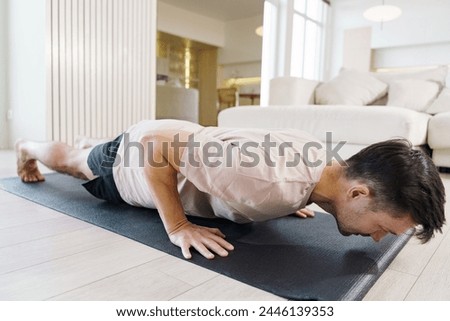 A man engages in a yoga push-up, focusing on core strength and stability in a tranquil, modern living space.

