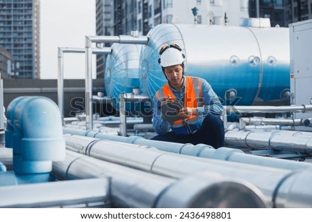Man engineer holding tablet working at rooftop building construction. Male technician worker working checking hvac of office building. Engineering installing large air conditioning system.