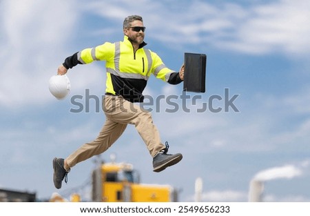 Man engineer running to success. Builder man run fast to work. Engineer supervisor running outdoor. Supervisor jumping. Excited builder construction worker jumping in front of trucks. Good job