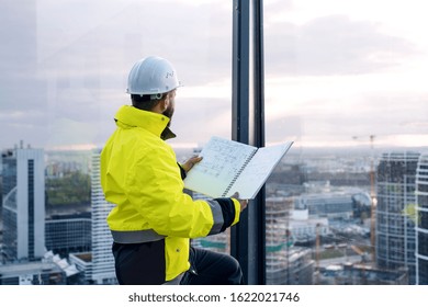 Man Engineer Standing On Construction Site, Holding Blueprints.