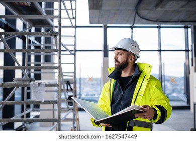 Man Engineer Standing On Construction Site, Holding Blueprints.