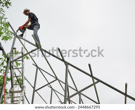 Man engineer standing on metal rail and using electric drill while installing support structure for photovoltaic solar panels. Isolated on white background.