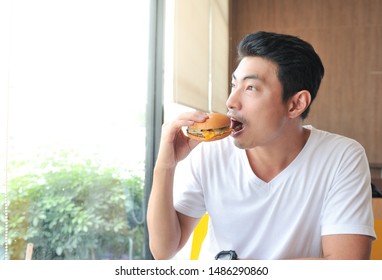 A Man Enjoy Eating With Her Burger In Hands,Asian Man Open His Mouth For Biting Burger,Men Eat Burgers Without Knowing The Danger Of Junk Food.,Selective Focus