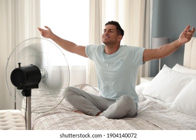 Hombre disfrutando del flujo de aire de un ventilador en la cama en la habitación. Calor de verano