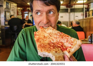 Man Enjoying A Large Slice Of Pizza In Local Eatery With A Look Of Delight On His Face.