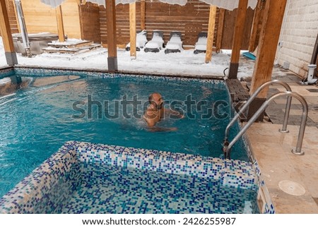 A man is enjoying a leisurely swim in a swimming pool filled with liquid water, surrounded by snowcovered wood building material and real estate