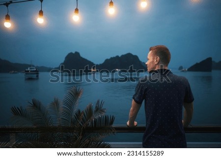 Man enjoying magnificent night view from cruise ship between islands. Popular tourist destination with karst formations in the sea, Ha Long Bay in Vietnam.
