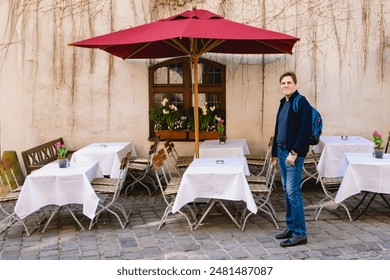 A man enjoying a moment at an outdoor cafe filled with red umbrellas, white tablecloths, and cobblestone ground. Munich, Germany. - Powered by Shutterstock