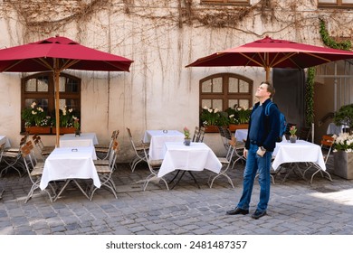 A man enjoying a moment at an outdoor cafe filled with red umbrellas, white tablecloths, and cobblestone ground. Munich, Germany. - Powered by Shutterstock