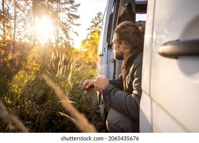 Man enjoying a morning coffee in the doorway of his camper van in autumn