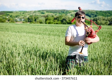 Man Enjoying Playing Pipes In Scotish Traditional Kilt On Green Outdoors Copy Space Summer Field. Male In Sunglasses