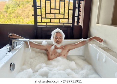 man is enjoying a relaxing bath as foam covers his head. The scene is set in a bathroom with a bathtub and a window, creating serene atmosphere. the guy relaxes in the bath on balcony at hotel. - Powered by Shutterstock