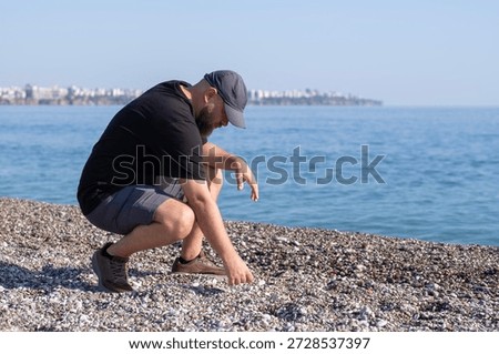 Man Enjoying Solitude While Throwing Stones into Water. Man Throwing Stones into the Sea. Peaceful Moment of a Man by the Sea. Relaxed Man Throwing Pebbles at the Shore.