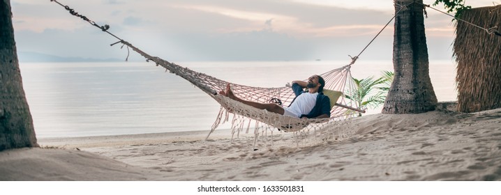 A man enjoys calm, lies in a hammock on the background of the ocean and sunset. Handsome guy meets the sunset on the beach of a tropical. Banner - Powered by Shutterstock