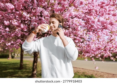 A man enjoys a coffee break while talking on his phone under vibrant pink cherry blossoms. This scene captures a peaceful moment of remote communication during the spring season. High quality photo