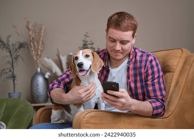 A man enjoys his smartphone, accompanied by his beagle, whose attention is drawn to the camera, a moment blending modern life with timeless companionship. - Powered by Shutterstock